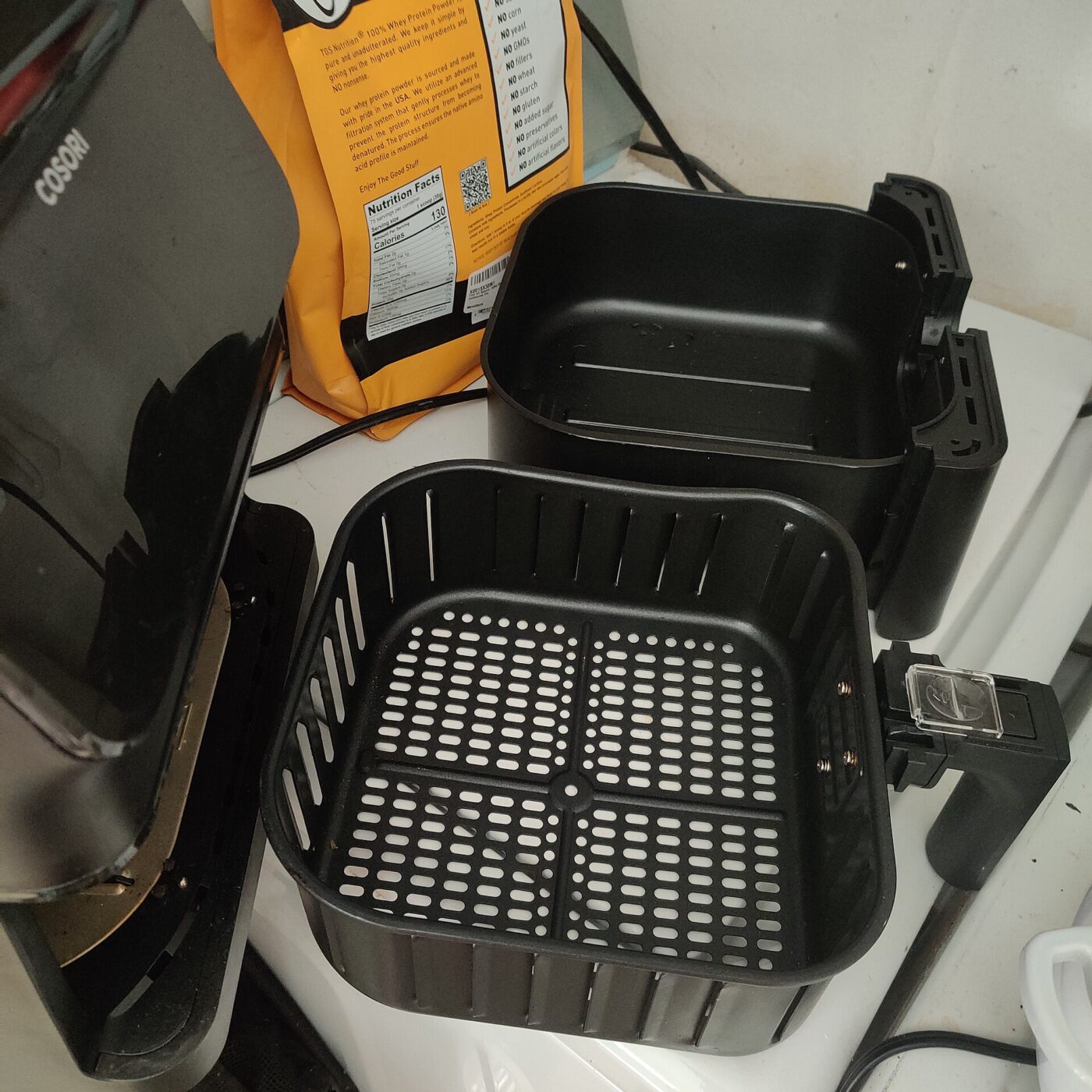 An air fryer basket with its perforated crisper plate removed and set beside it