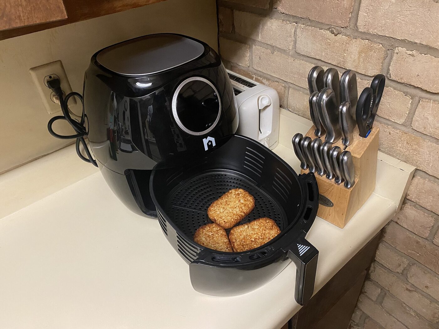 A black air fryer on a kitchen counter beside a knife block, basket open