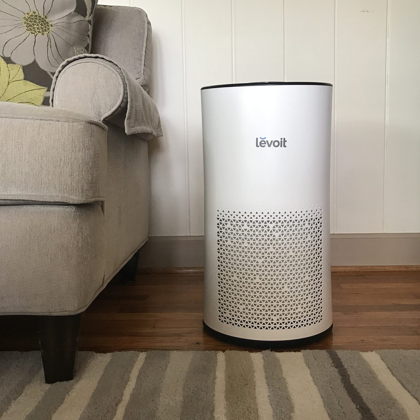 A Levoit air purifier on the floor beside a sofa.
