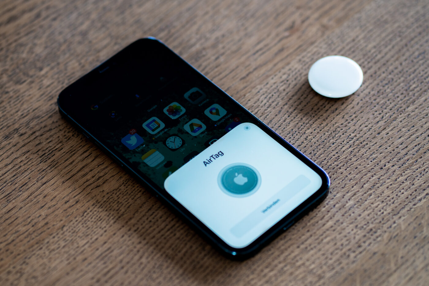 A phone with an AirTag pairing screen next to a small white AirTag disc.