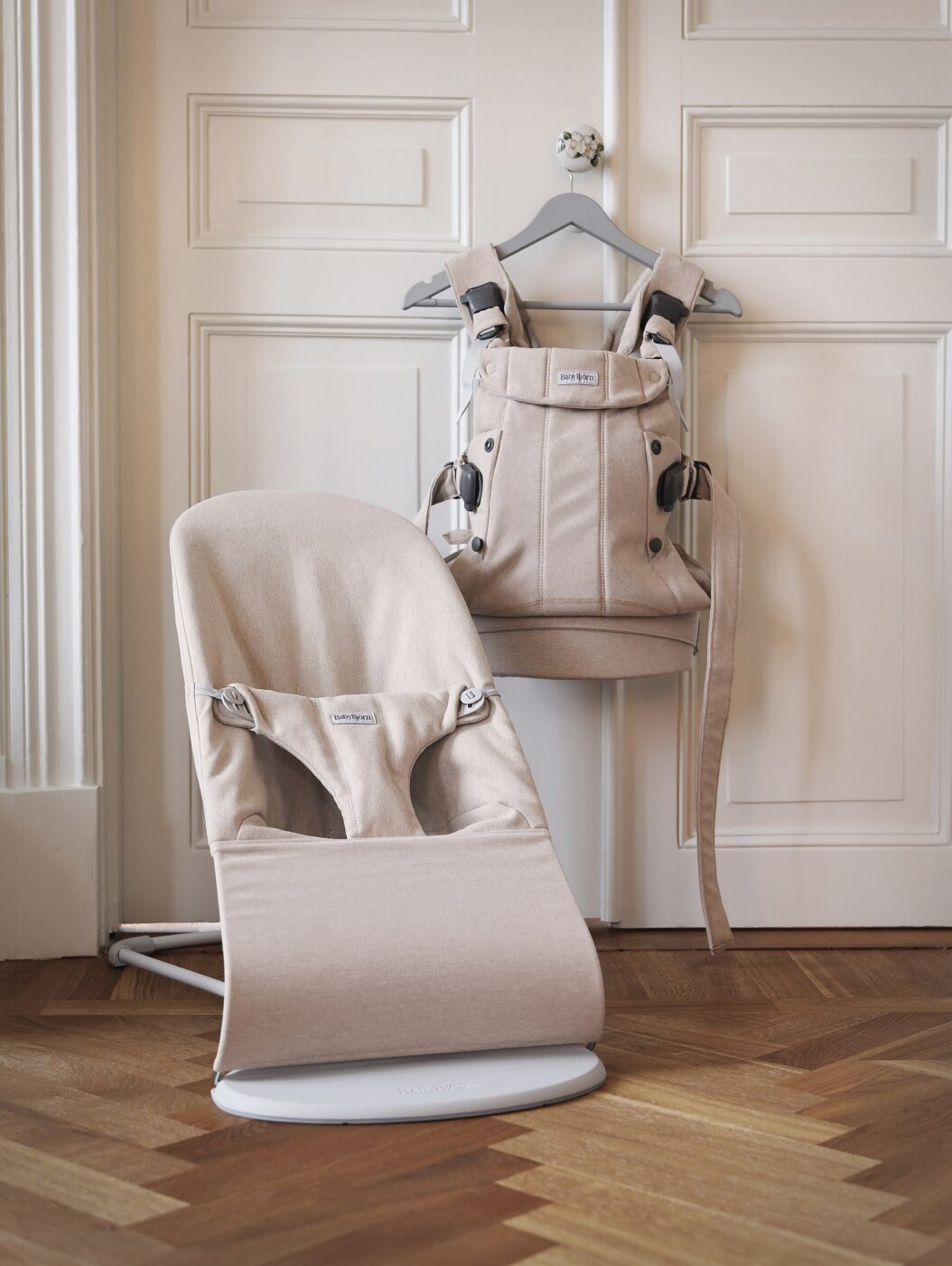 An empty soft structured baby carrier hanging by its straps, showing its wide seat panel.