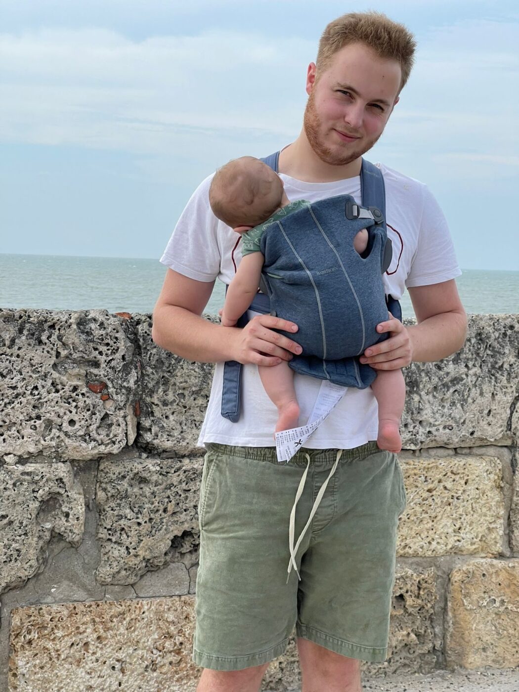 A parent wearing a soft structured baby carrier, the baby's legs spread wide.