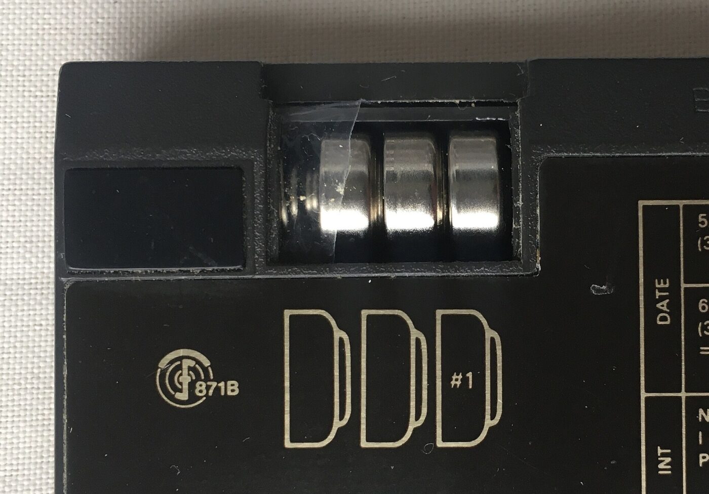 Open device compartment showing three round button-cell batteries loaded inside an old calculator.