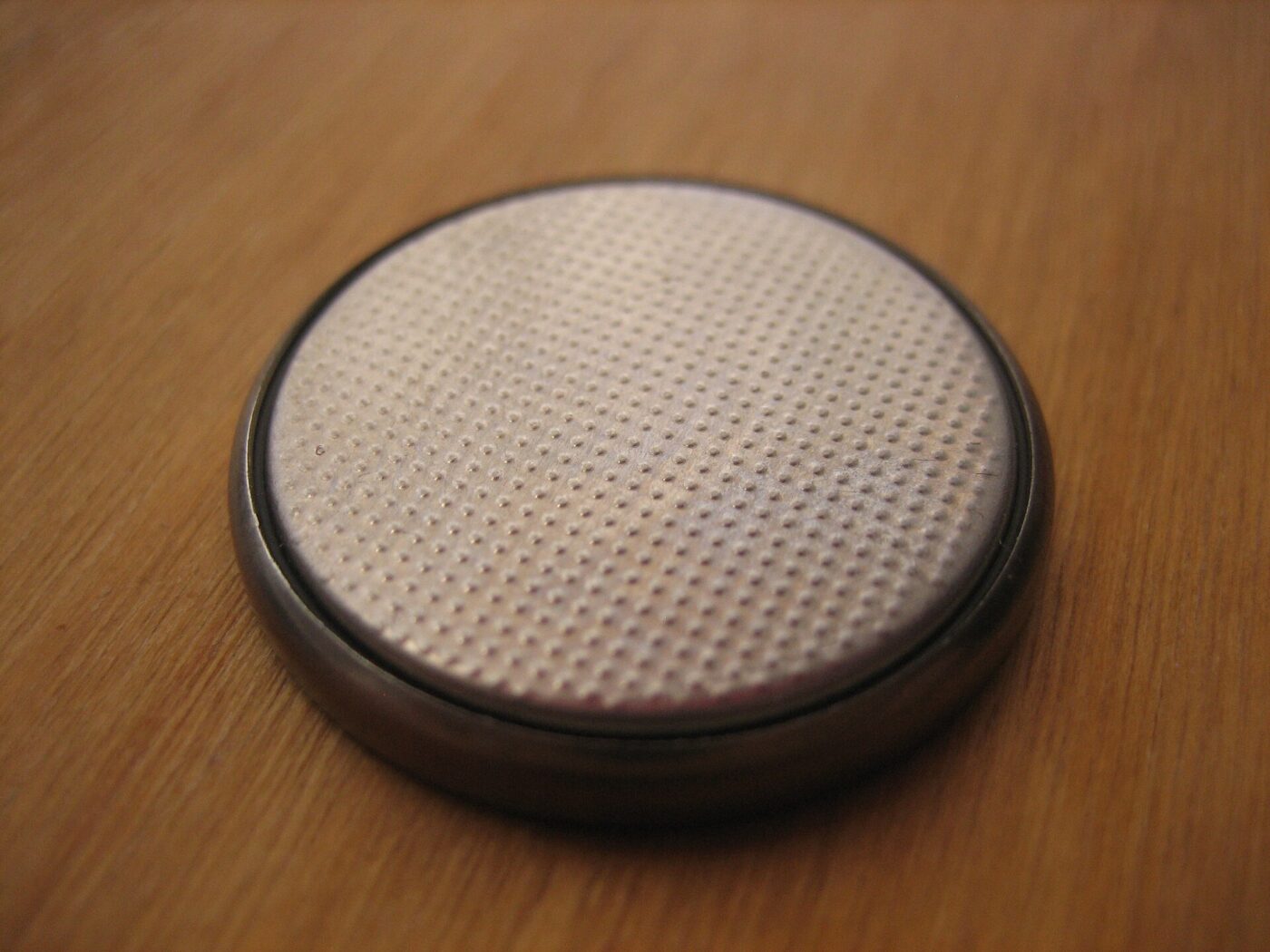 Close-up of one round silver button-cell battery resting on a wooden tabletop.