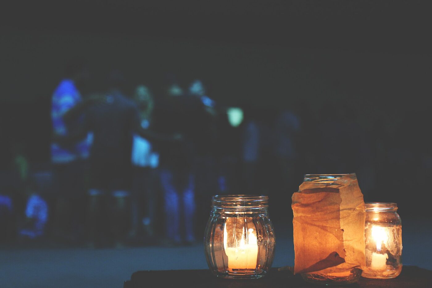 Several lit candles in different glass containers glowing at dusk.