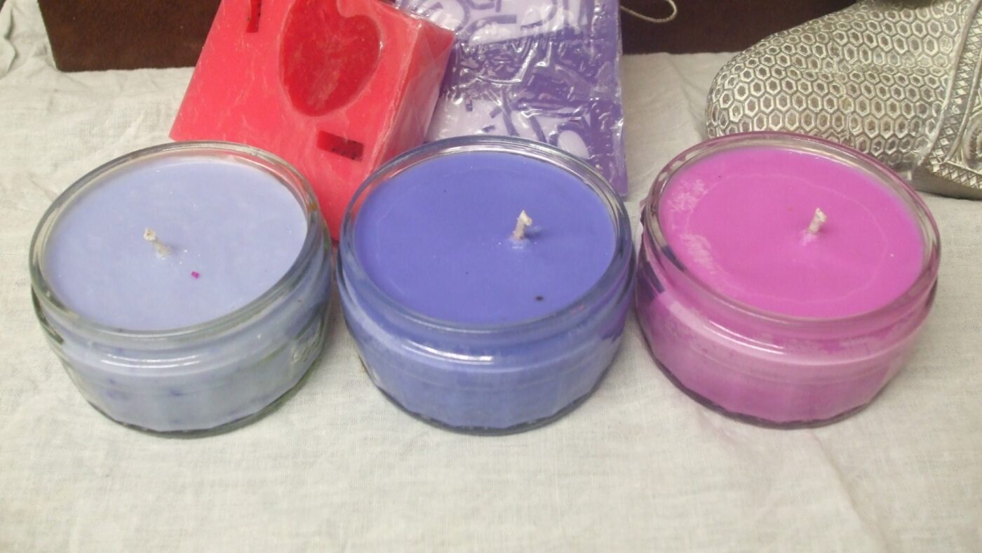 Three candles in tins of different colors with visible wicks, side by side.