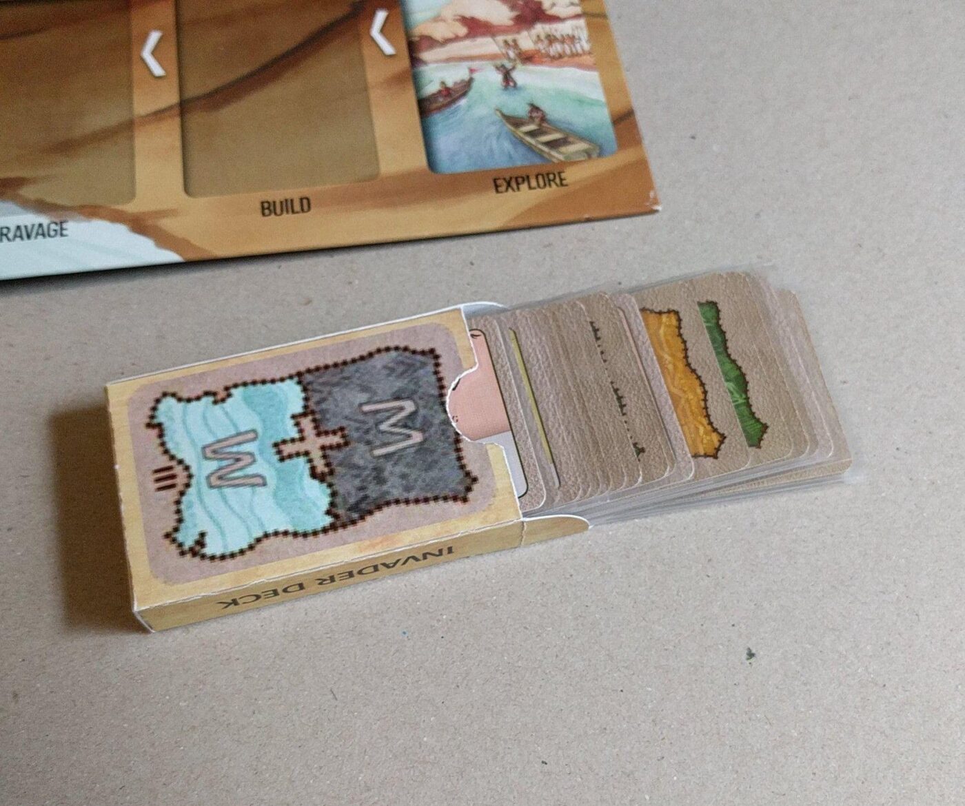 A cardboard tuck box for a board game holding a stacked deck of cards.