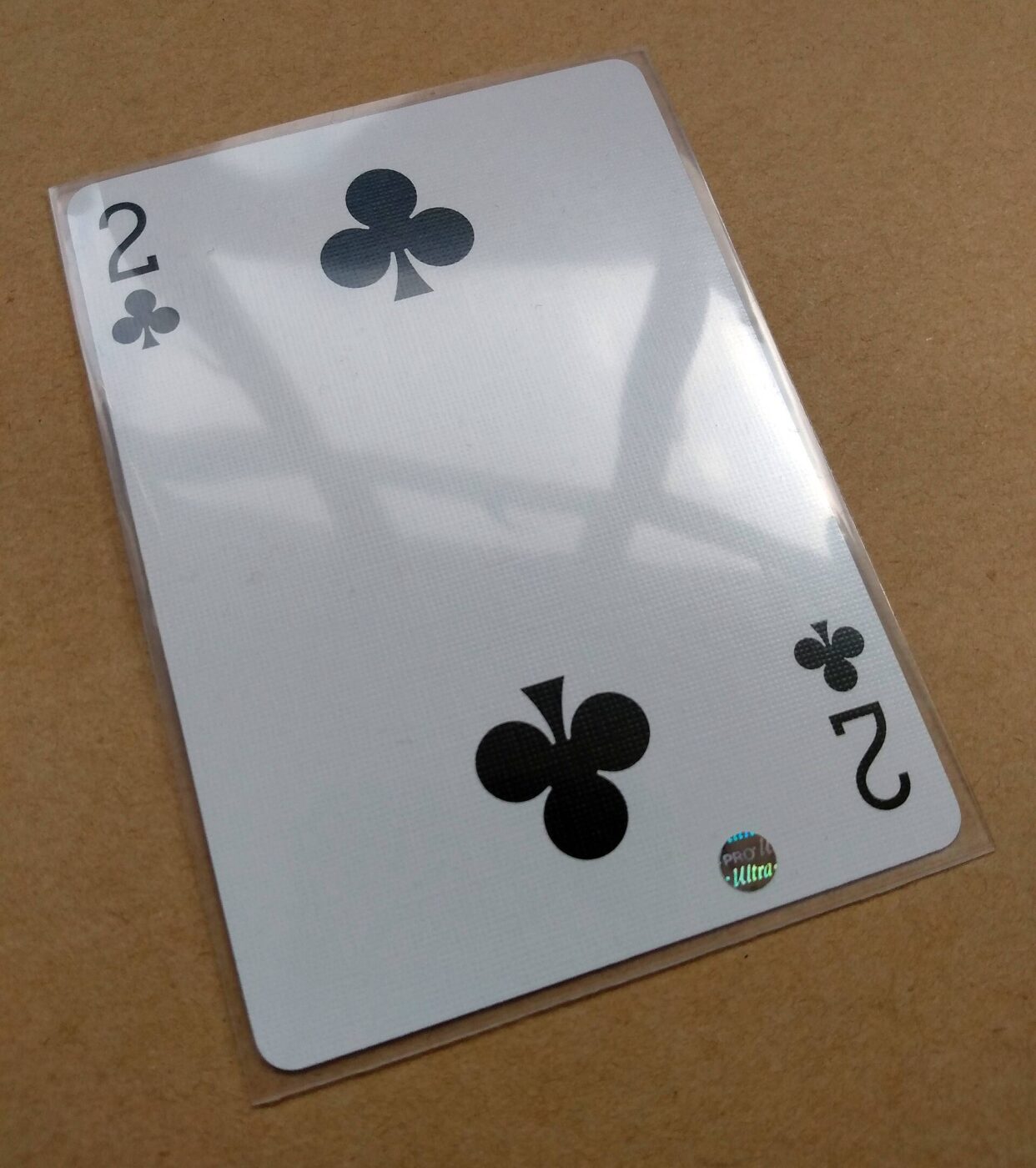 A two of clubs playing card enclosed in a clear protective plastic sleeve.