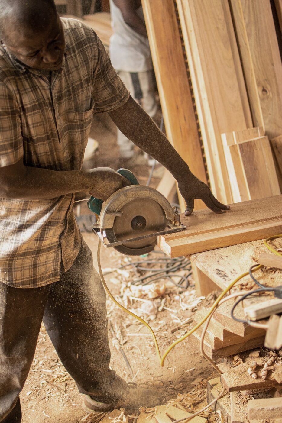 A carpenter cuts a wood panel with a circular saw, sawdust flying.