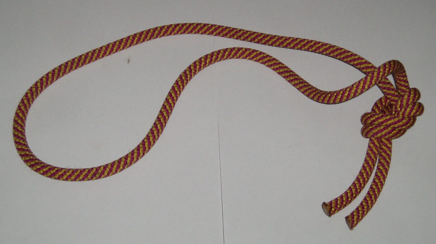 A red and black climbing rope coiled and knotted against a plain background.