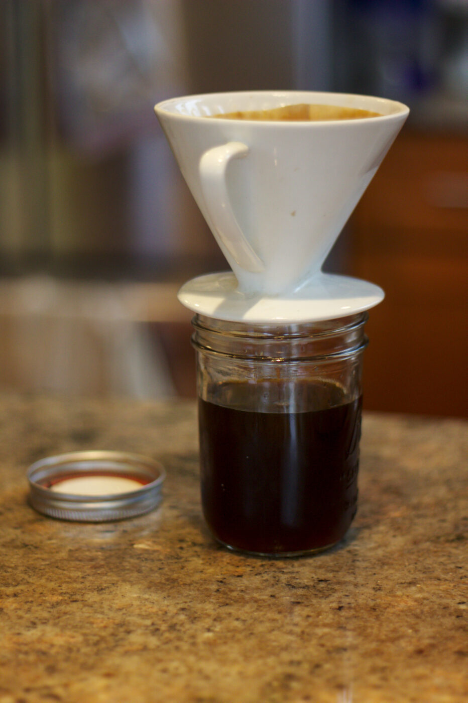 White ceramic filter cone straining cold brew coffee concentrate into a glass mason jar.