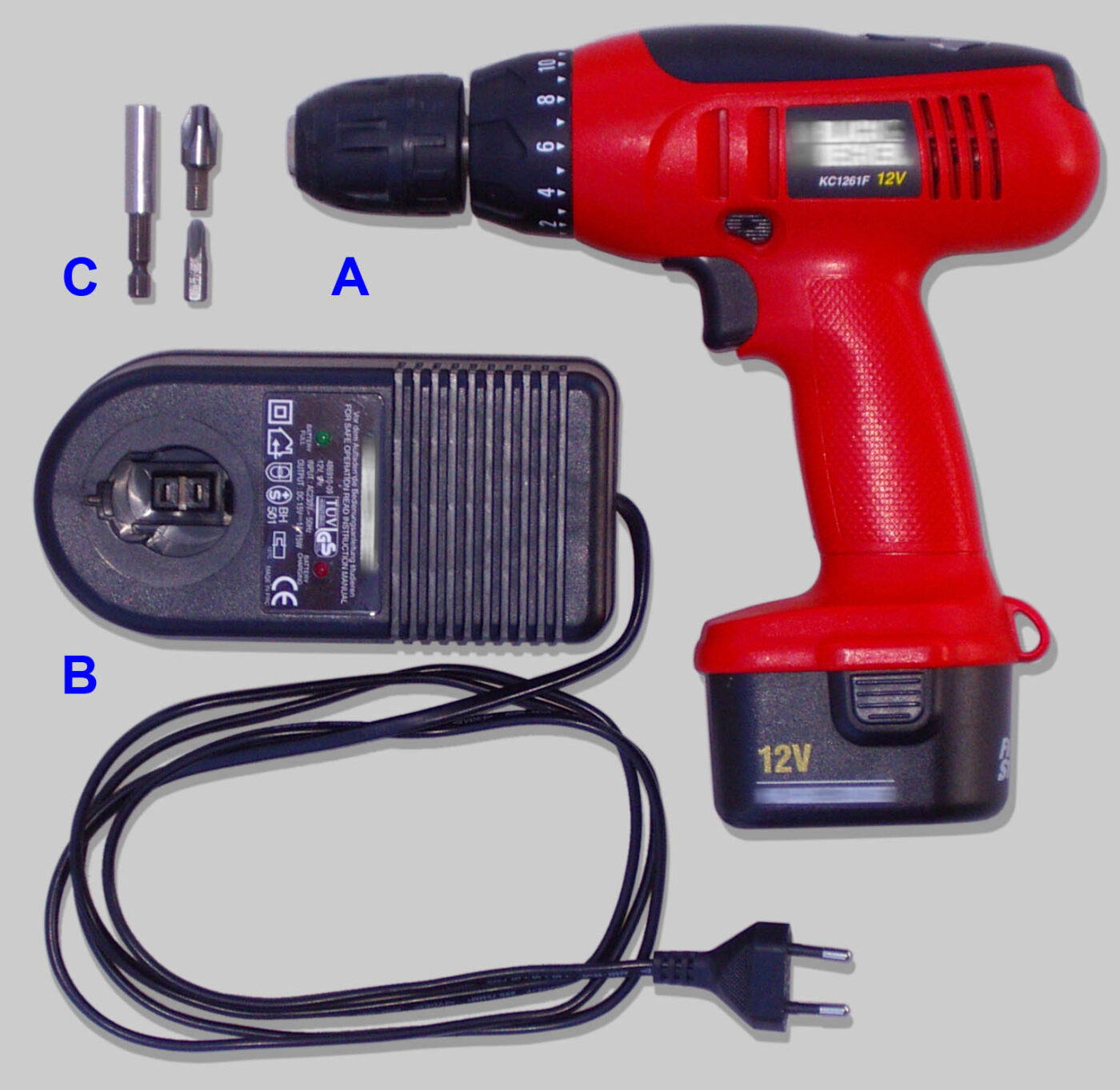 A cordless drill kit laid out: drill with battery, charger, and driver bits