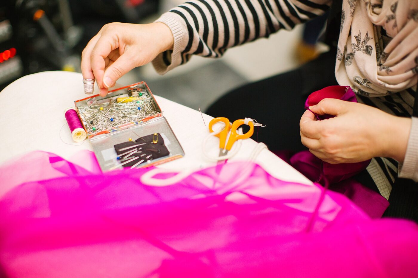 Close-up of hands sewing pink fabric with scissors and pins nearby.