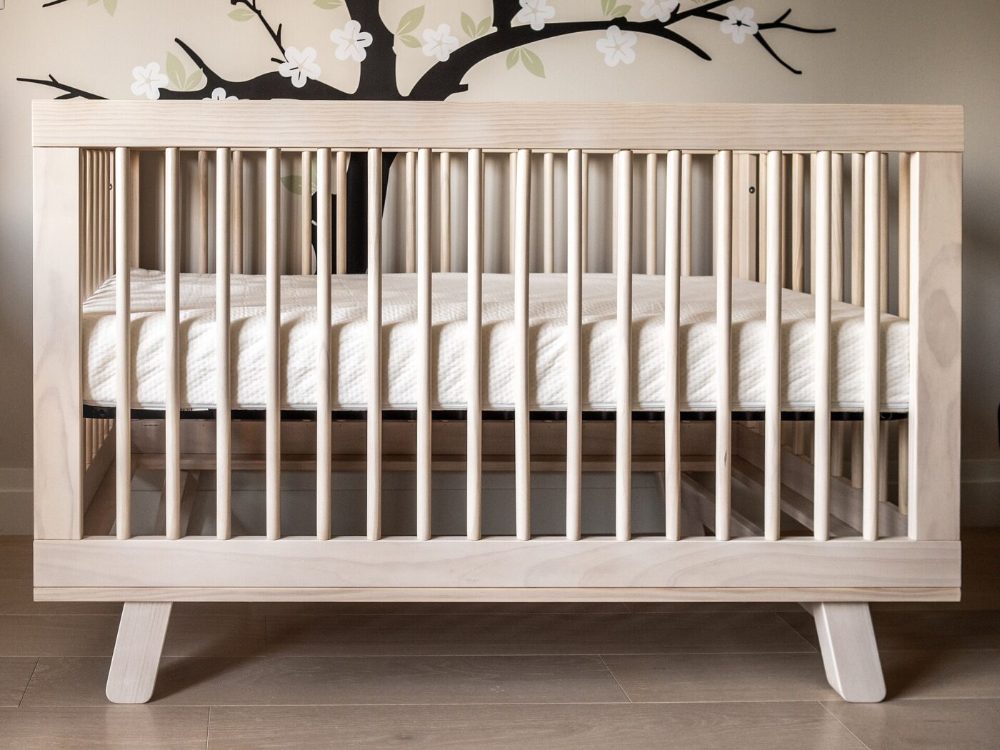 An empty modern crib with a bare mattress and wood slats.