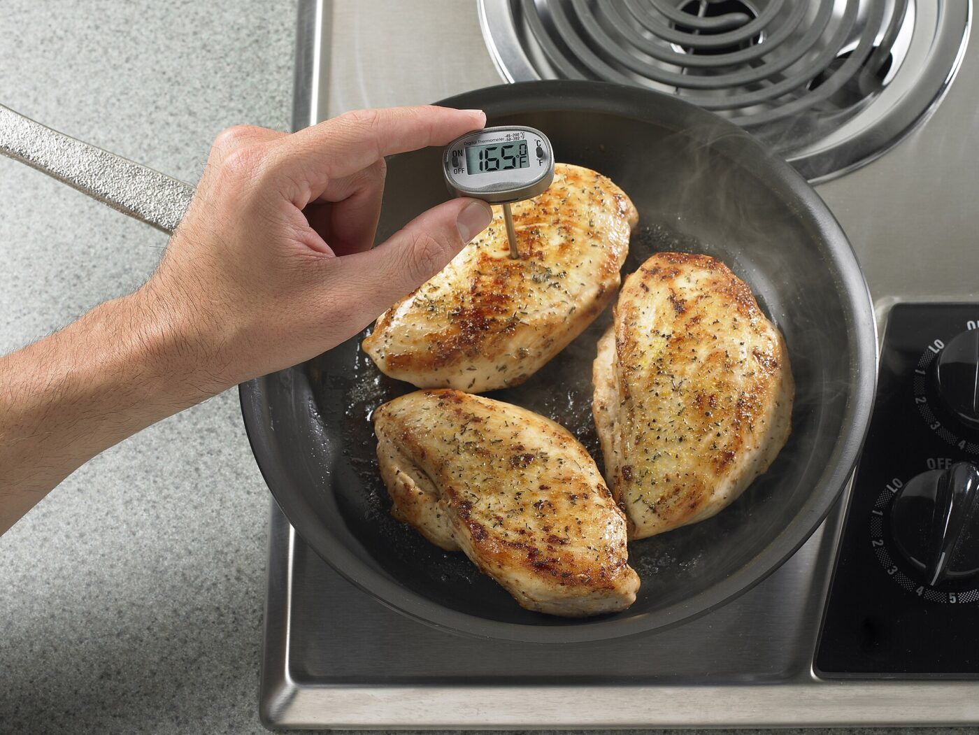 Digital food thermometer checking the temperature of cooked chicken breasts in a pan.