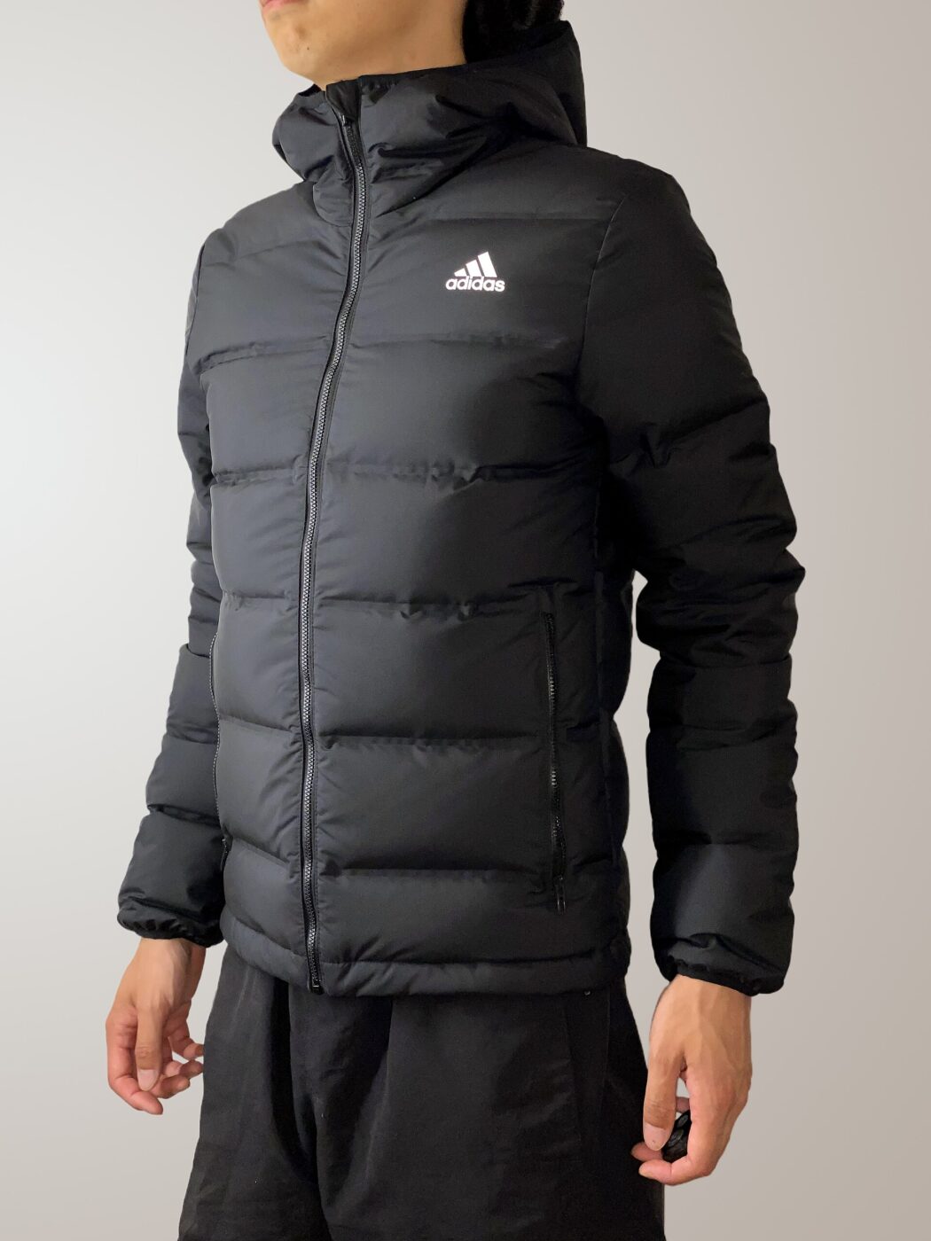 Studio photo of a person wearing a black Adidas quilted down jacket.