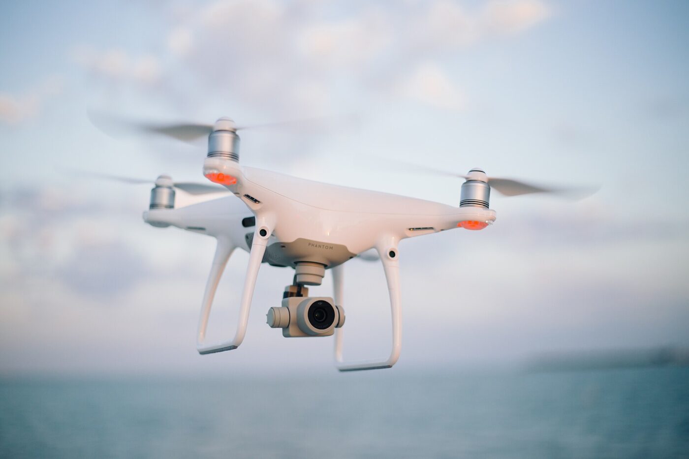 White quadcopter drone with an onboard camera flying just above the water.