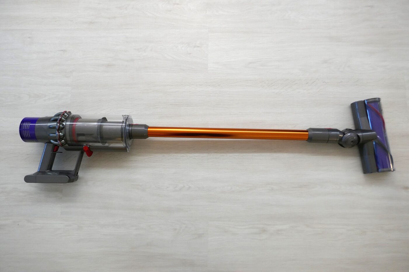 Dyson V6 cordless stick vacuum, grey and purple body, standing upright on a light wood floor.