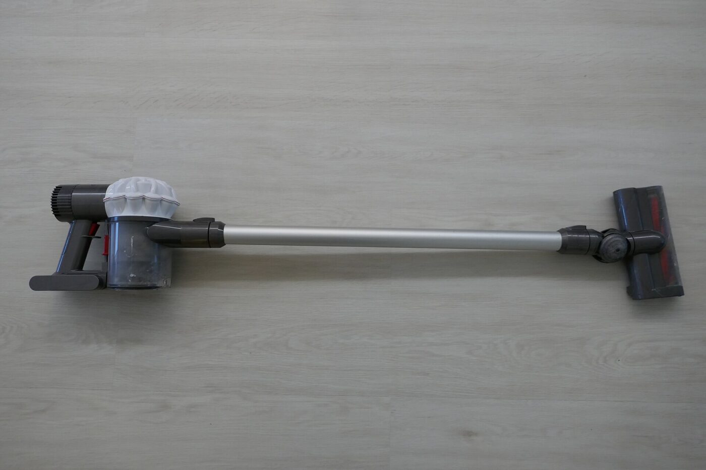 Dyson Cyclone V10 Absolute cordless stick vacuum with orange wand and clear dust bin, standing on a wood floor.