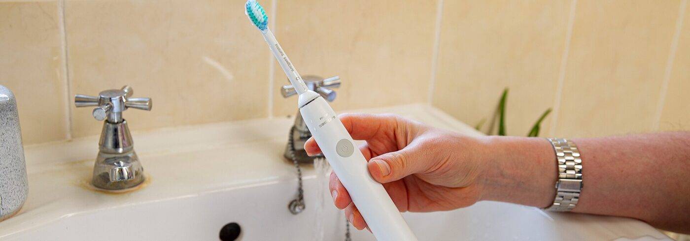 A Philips Sonicare electric toothbrush being rinsed at the sink.