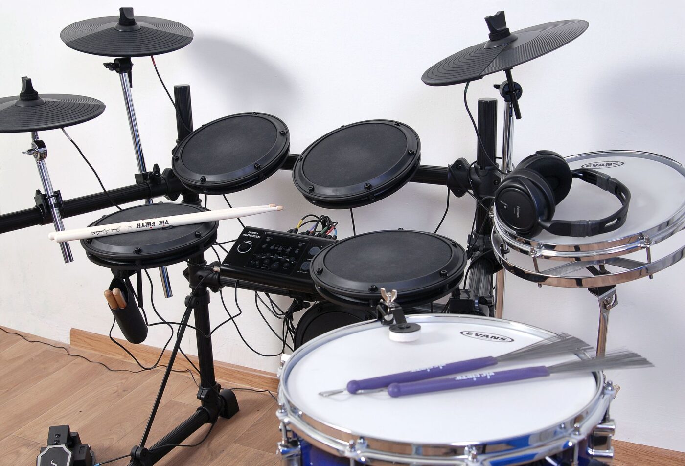 An electronic drum kit with rubber mesh pads, cymbals and a rack sitting on hardwood flooring.