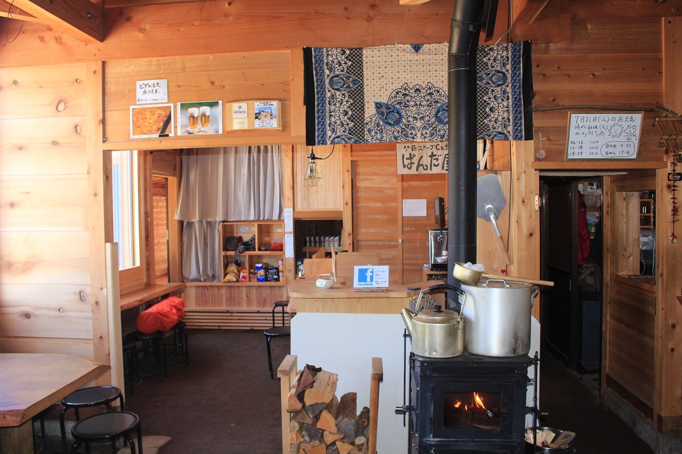 Black wood-burning stove with a stainless flue pipe inside a wood-paneled cabin room.
