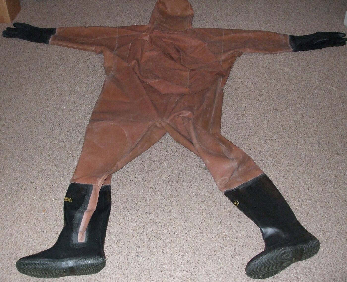 One-piece chest-high wader suit with rubber boots and gloves spread out on a surface.
