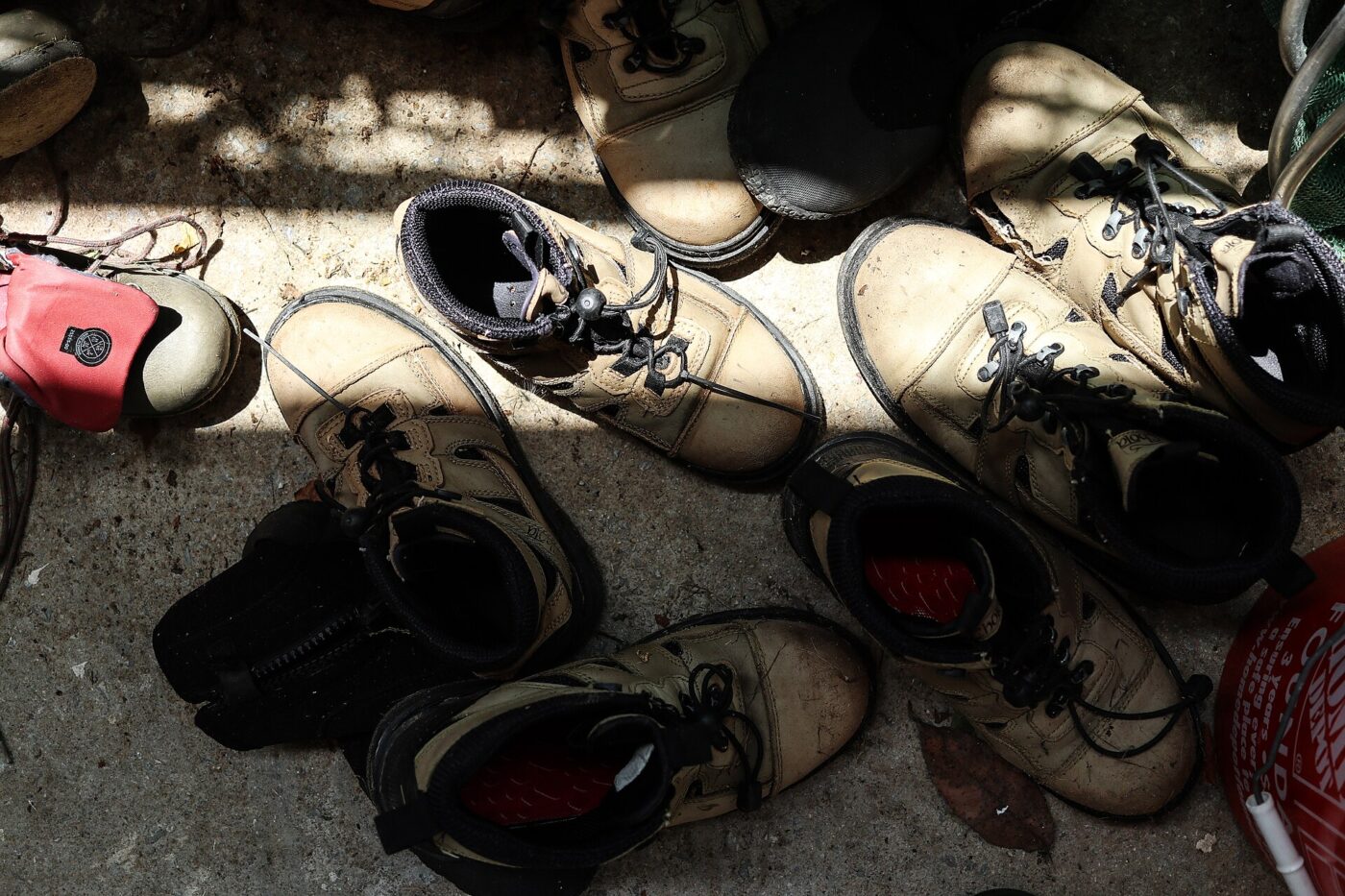 Row of worn, mud-covered wading boots drying on the ground.