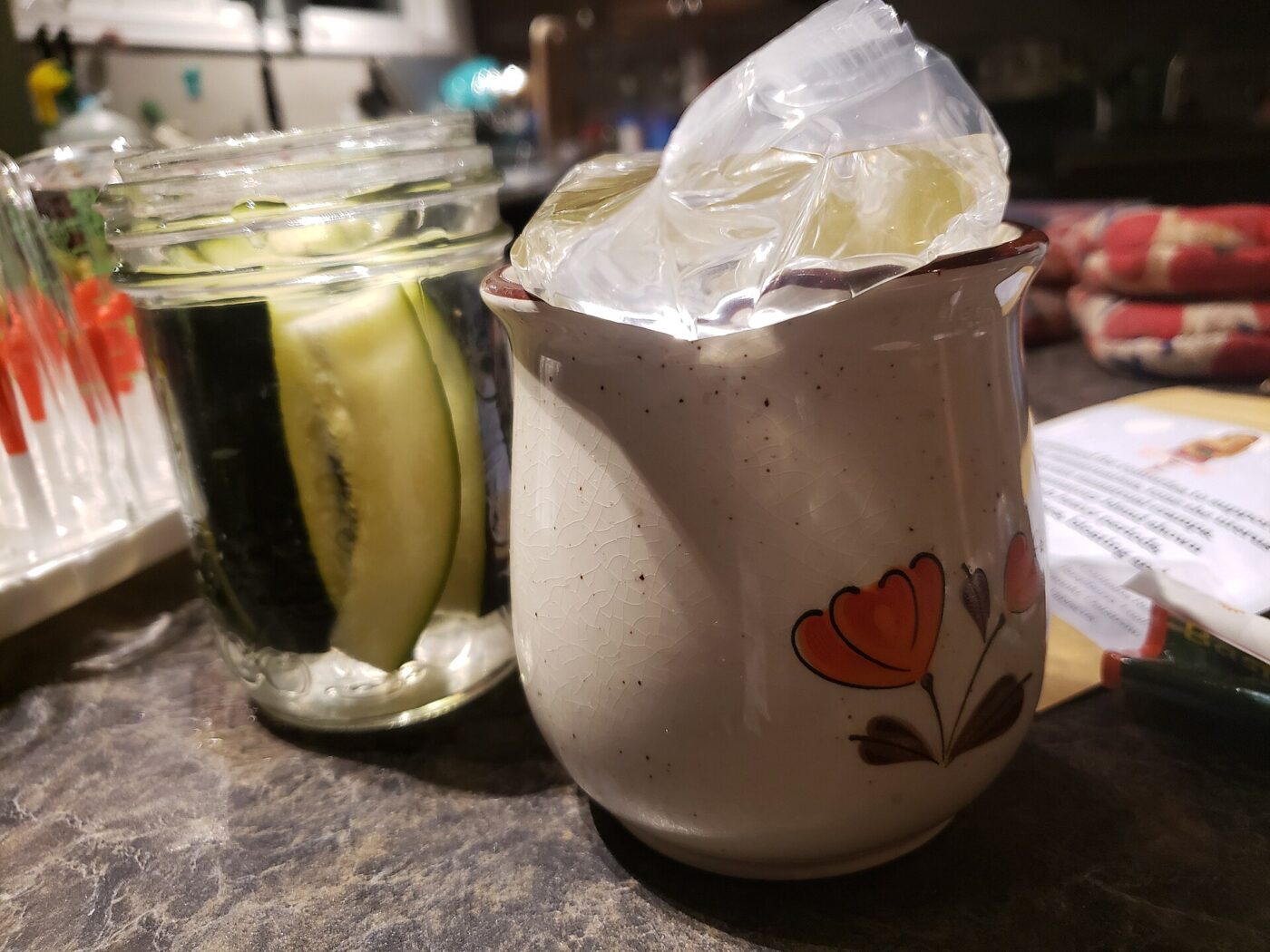 Mason jar holding fermenting cucumbers with a cloth-wrapped weight on top.