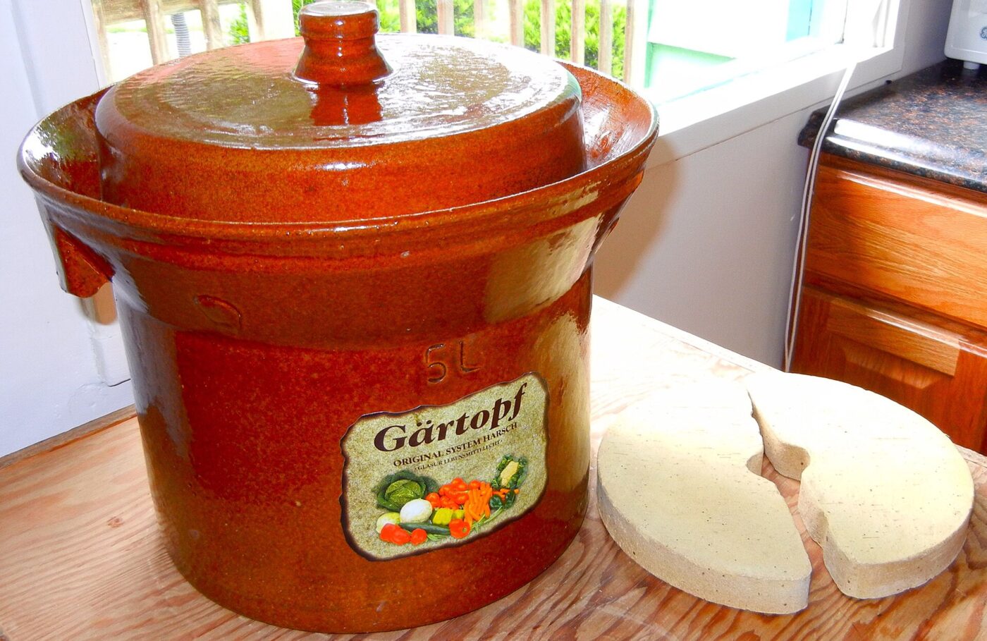 Reddish ceramic fermentation crock with a lid and two round ceramic weights.