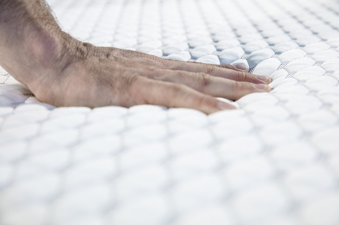 A hand pressing into a white quilted mattress surface.