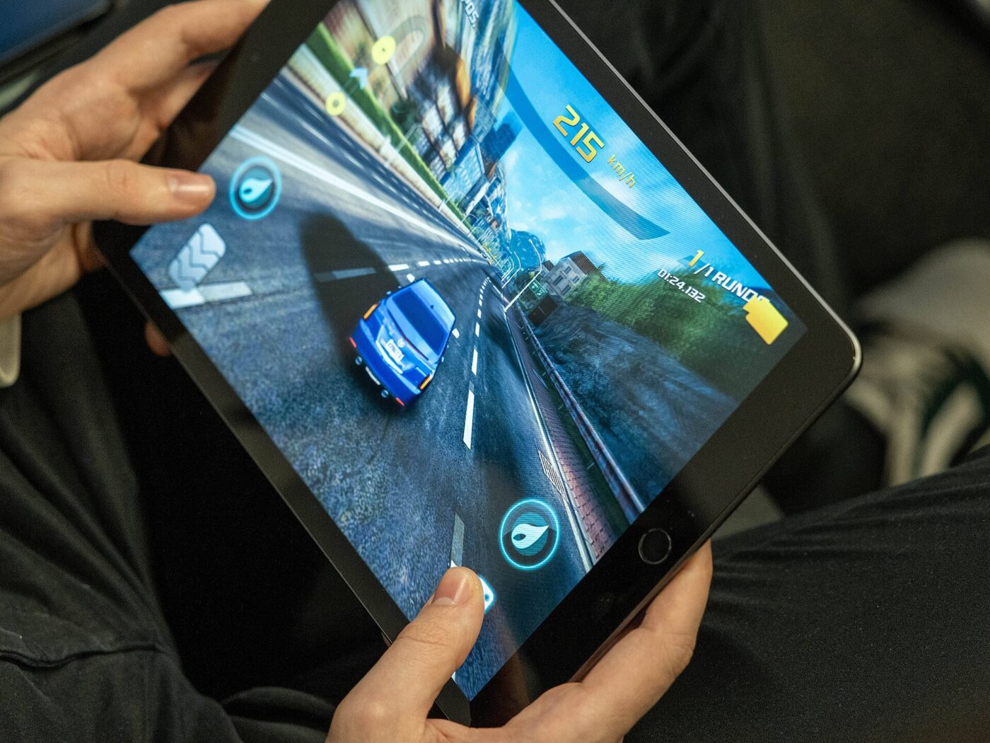 Arms and hands holding a tablet displaying a colorful game.
