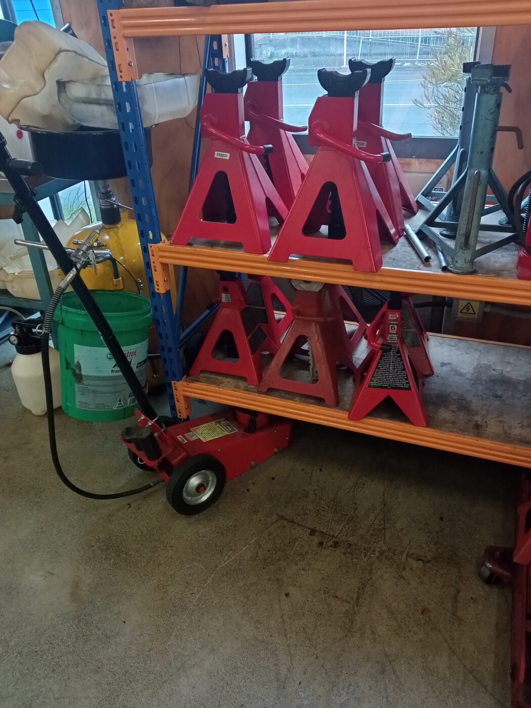 A hydraulic trolley jack next to a set of red axle stands in a garage.