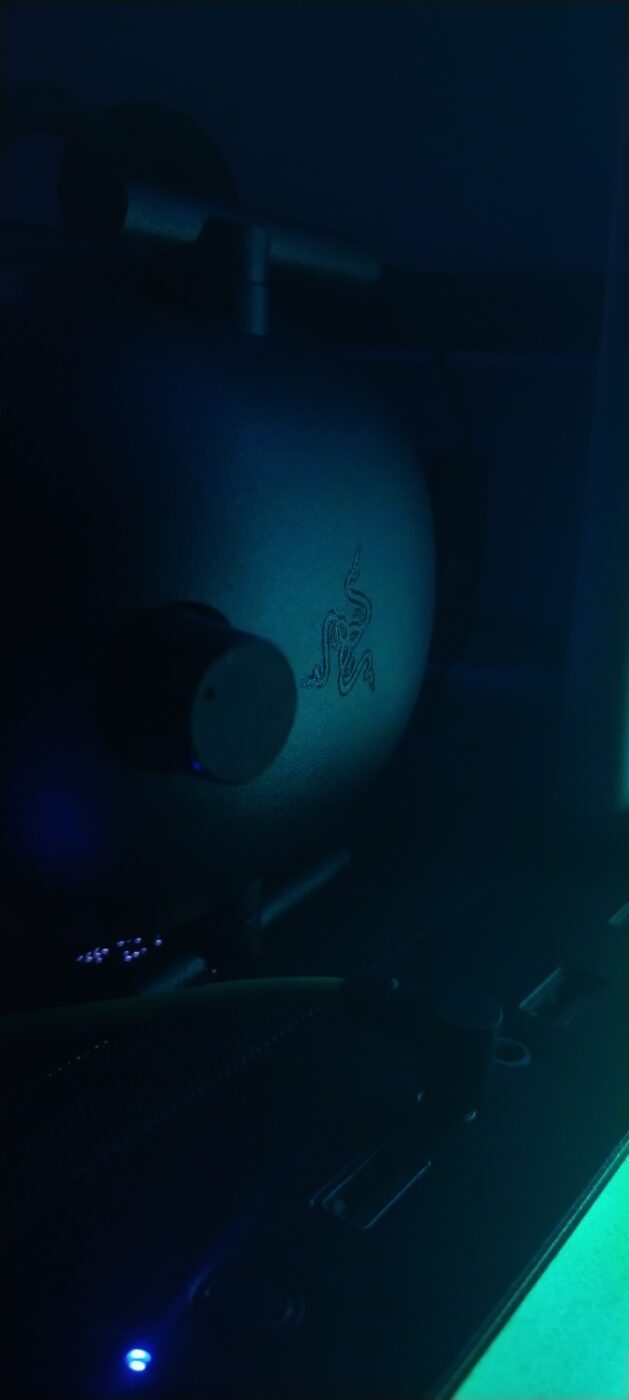 Black gaming headset with RGB accent lighting on a computer desk, no people in frame.