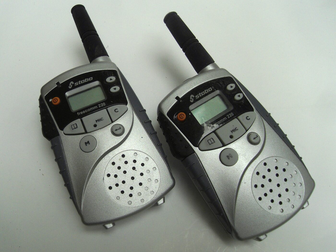 Two silver handheld walkie-talkie radios with antennas raised, standing upright on a gray surface.
