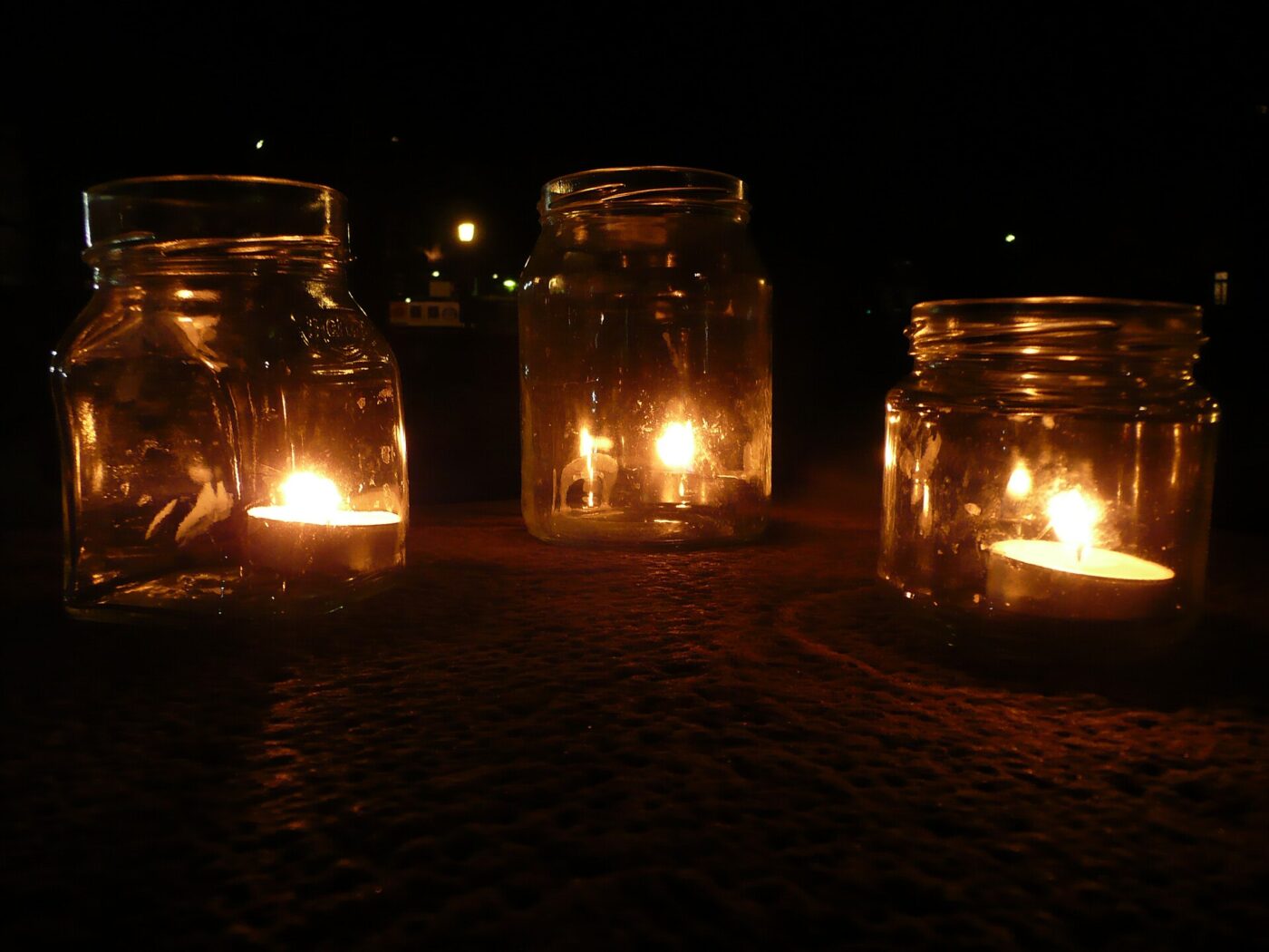 Three tealight candles burning inside glass jars.
