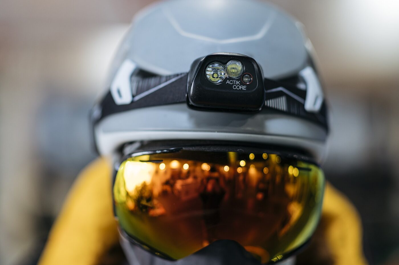 A headlamp strapped to a climbing helmet above ski goggles.