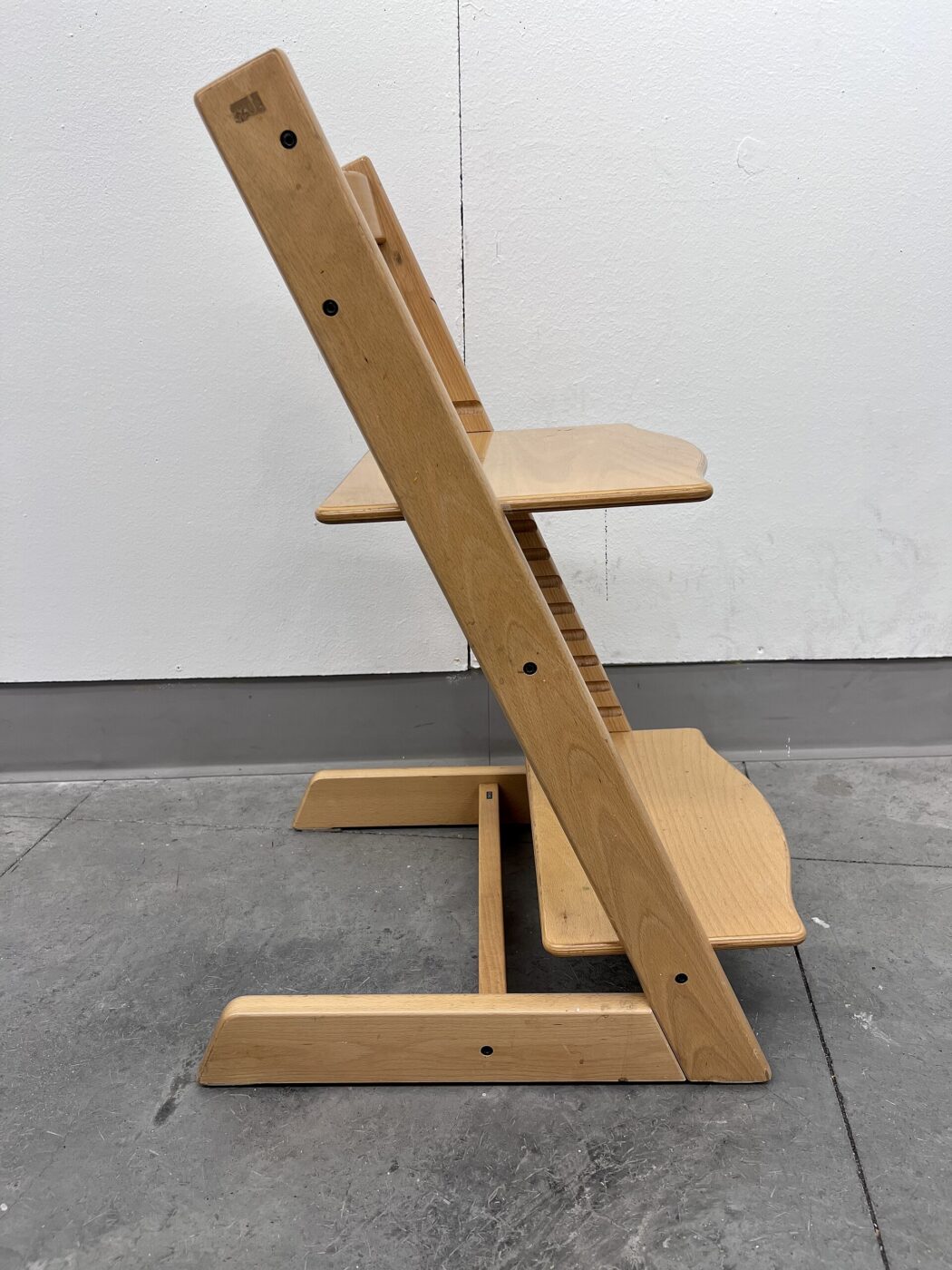 An empty modern adjustable wooden high chair against a plain background.