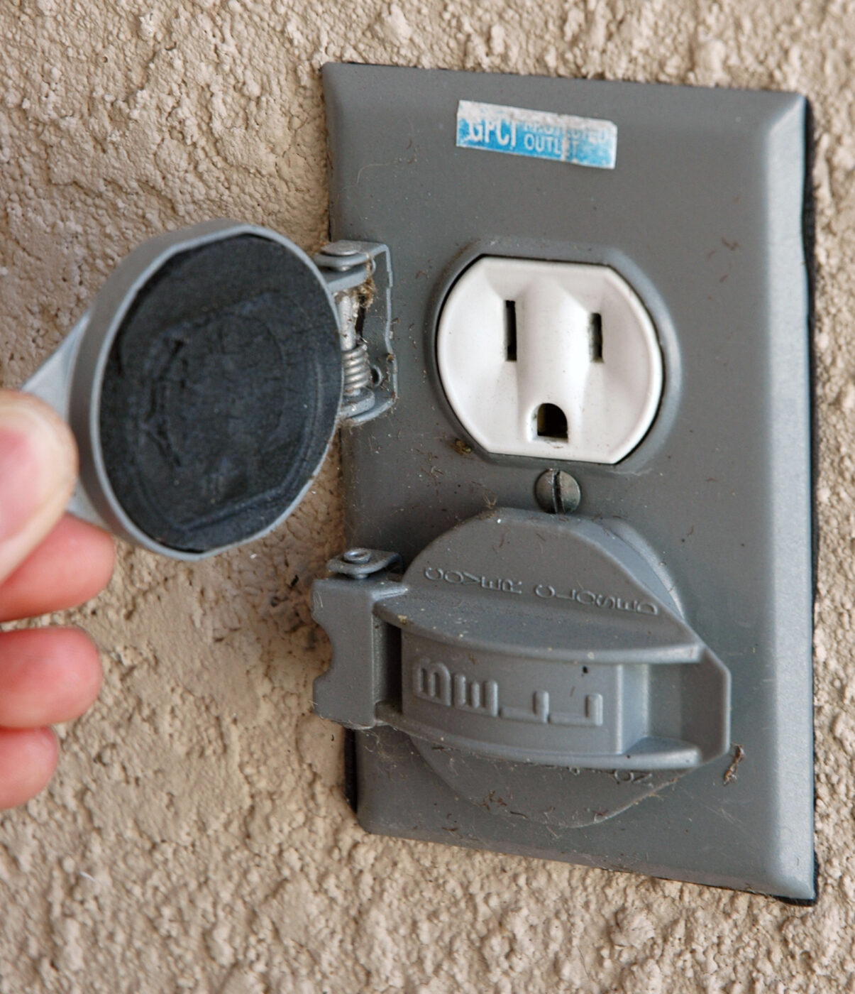 Close-up of a gray outdoor GFCI outlet with its weatherproof cover lifted open.