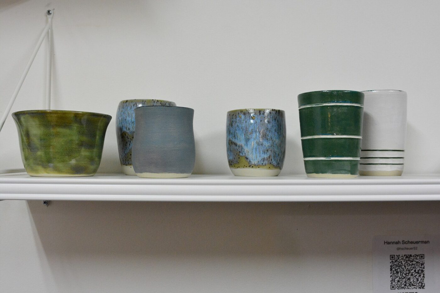 A shelf of handmade ceramic cups in varied glazes