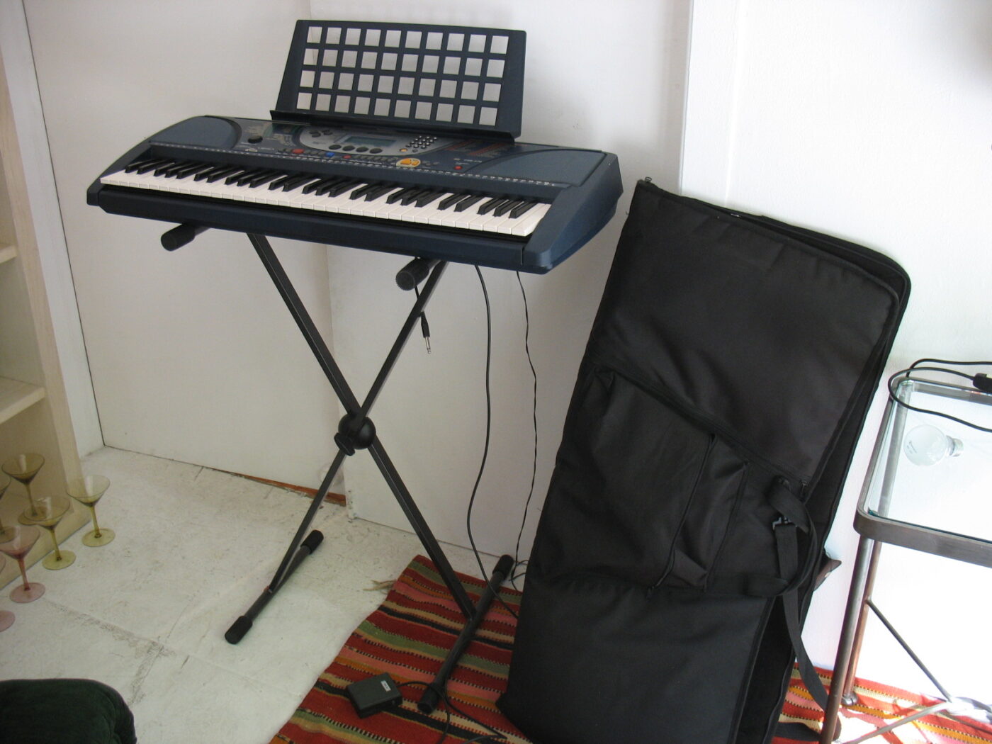 Yamaha 61-key portable keyboard on a stand, with its soft carrying case behind it.