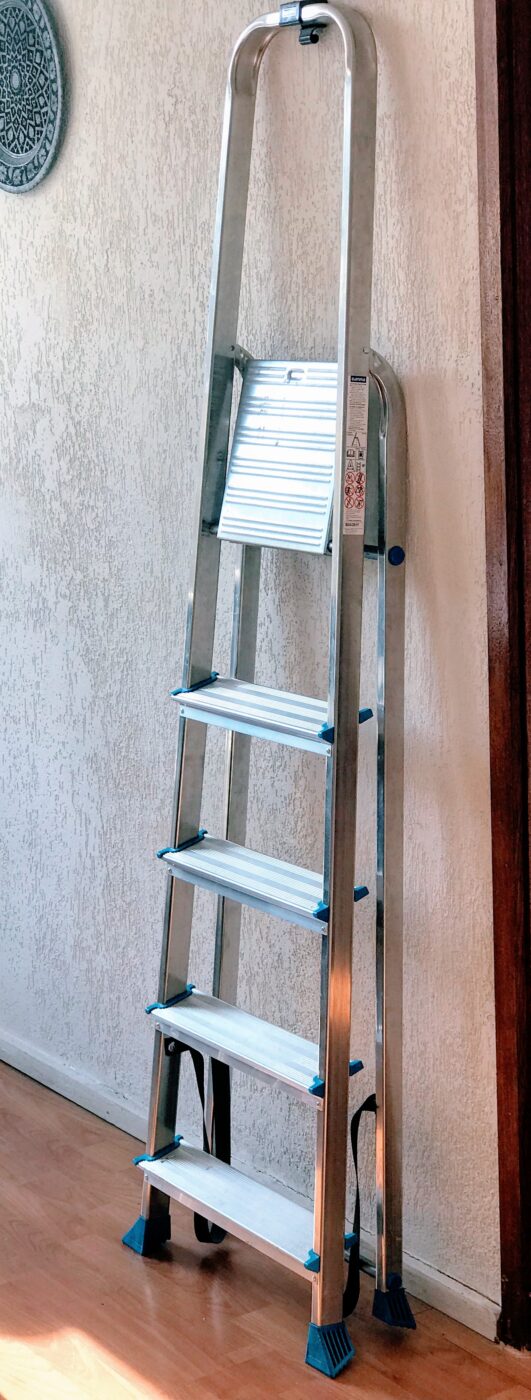 A folded aluminium step ladder standing against a wall.