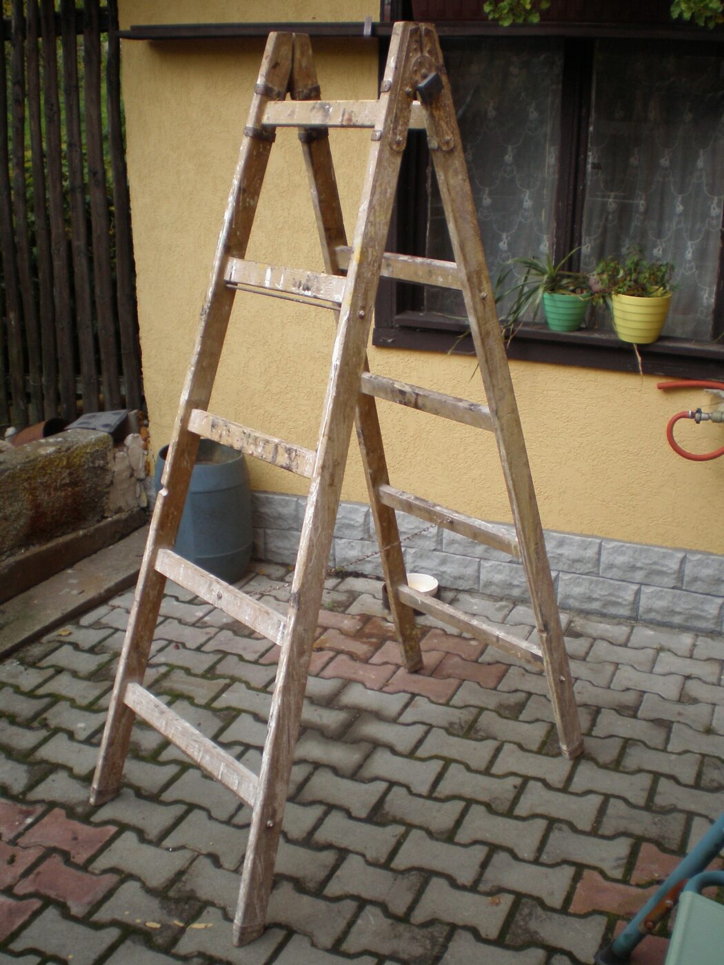 A worn wooden A-frame ladder set up on a paved patio.