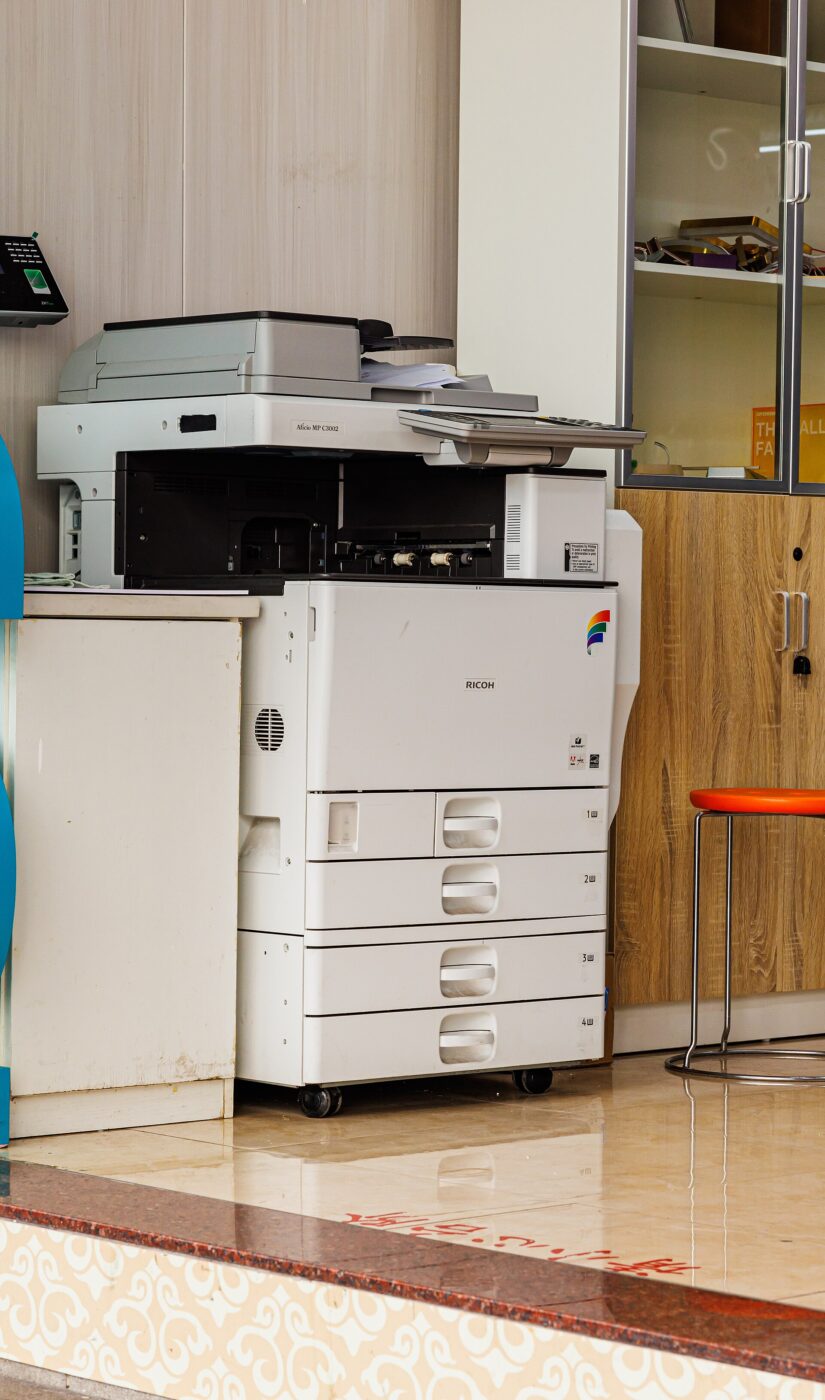 A Ricoh multifunction laser printer standing in an office.