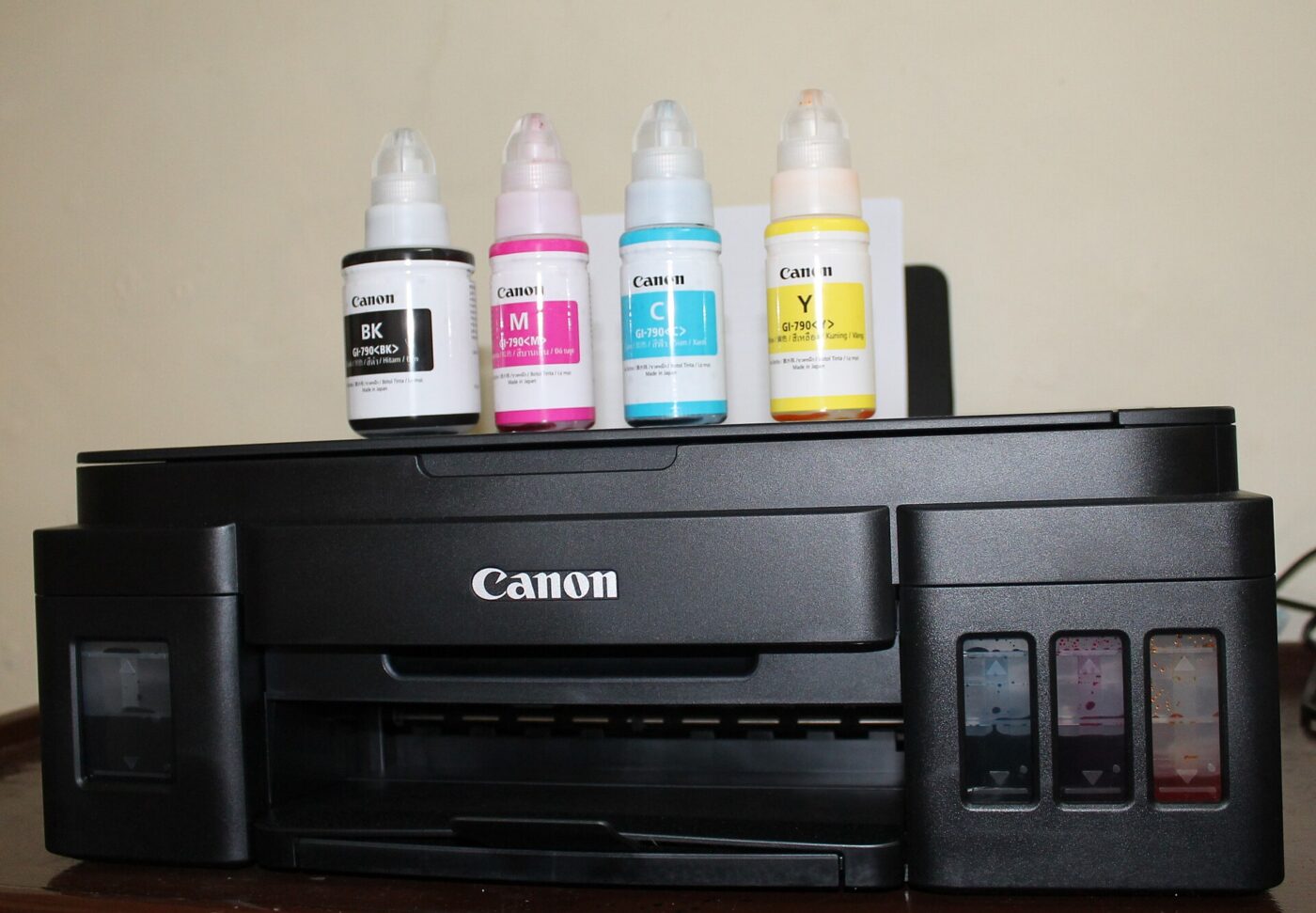 A Canon ink-tank printer with refill bottles on top.