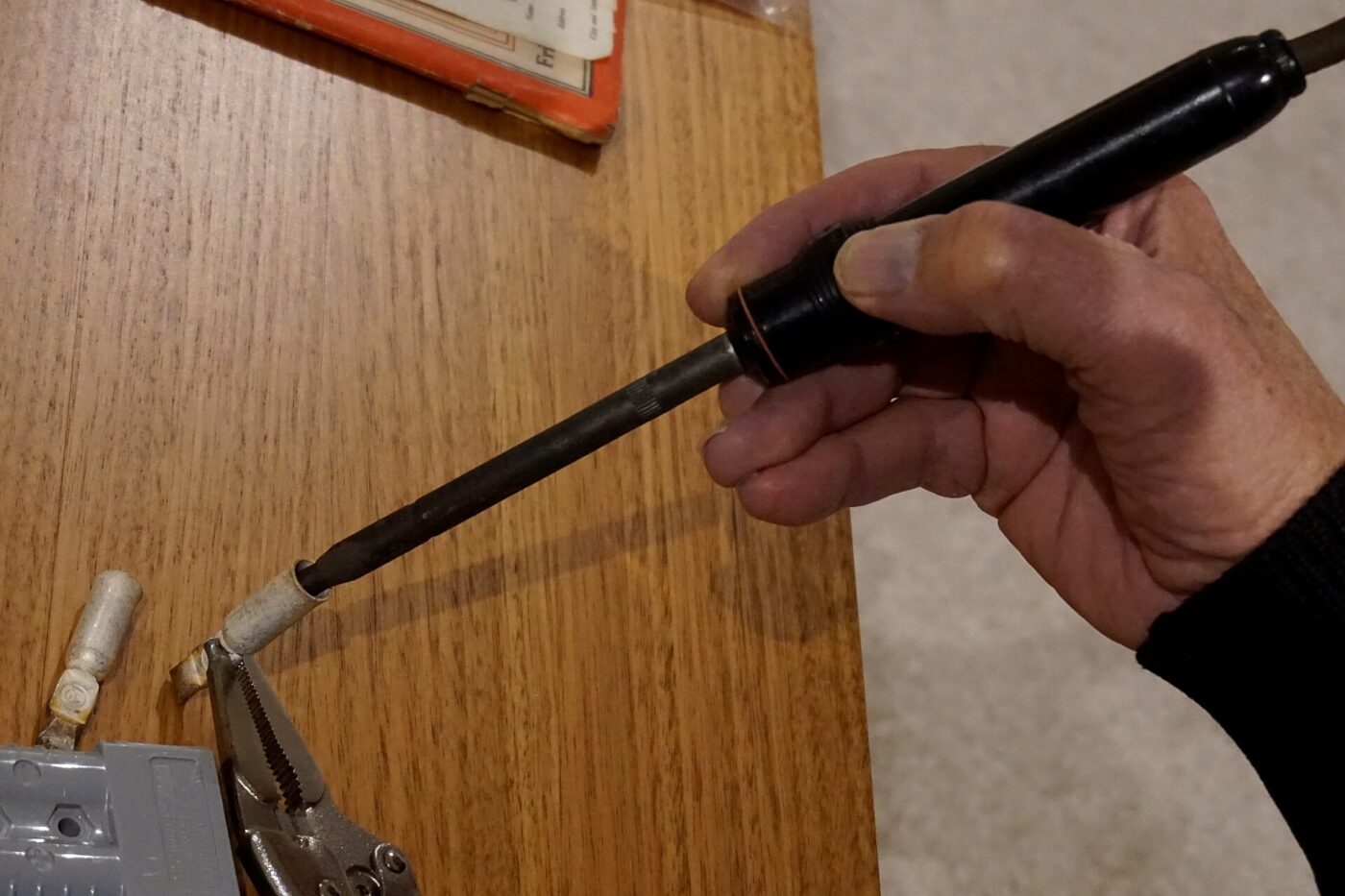 A hand holding a soldering iron while working on a circuit board on a workbench.
