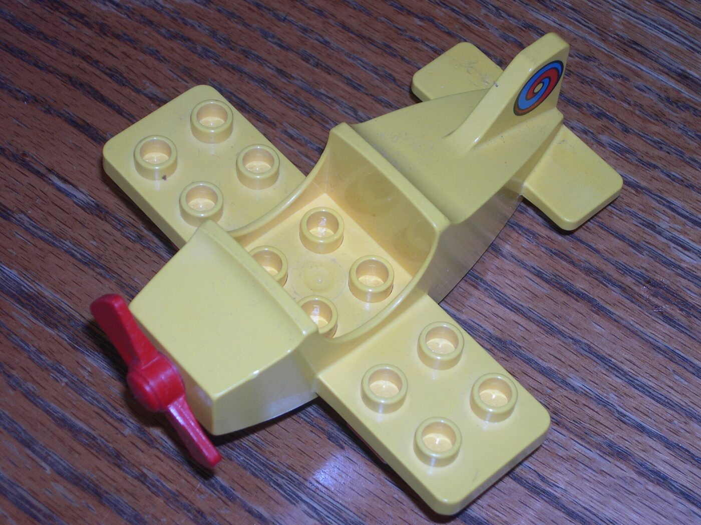 A tan LEGO airplane piece with round connector studs sitting on a wood table.