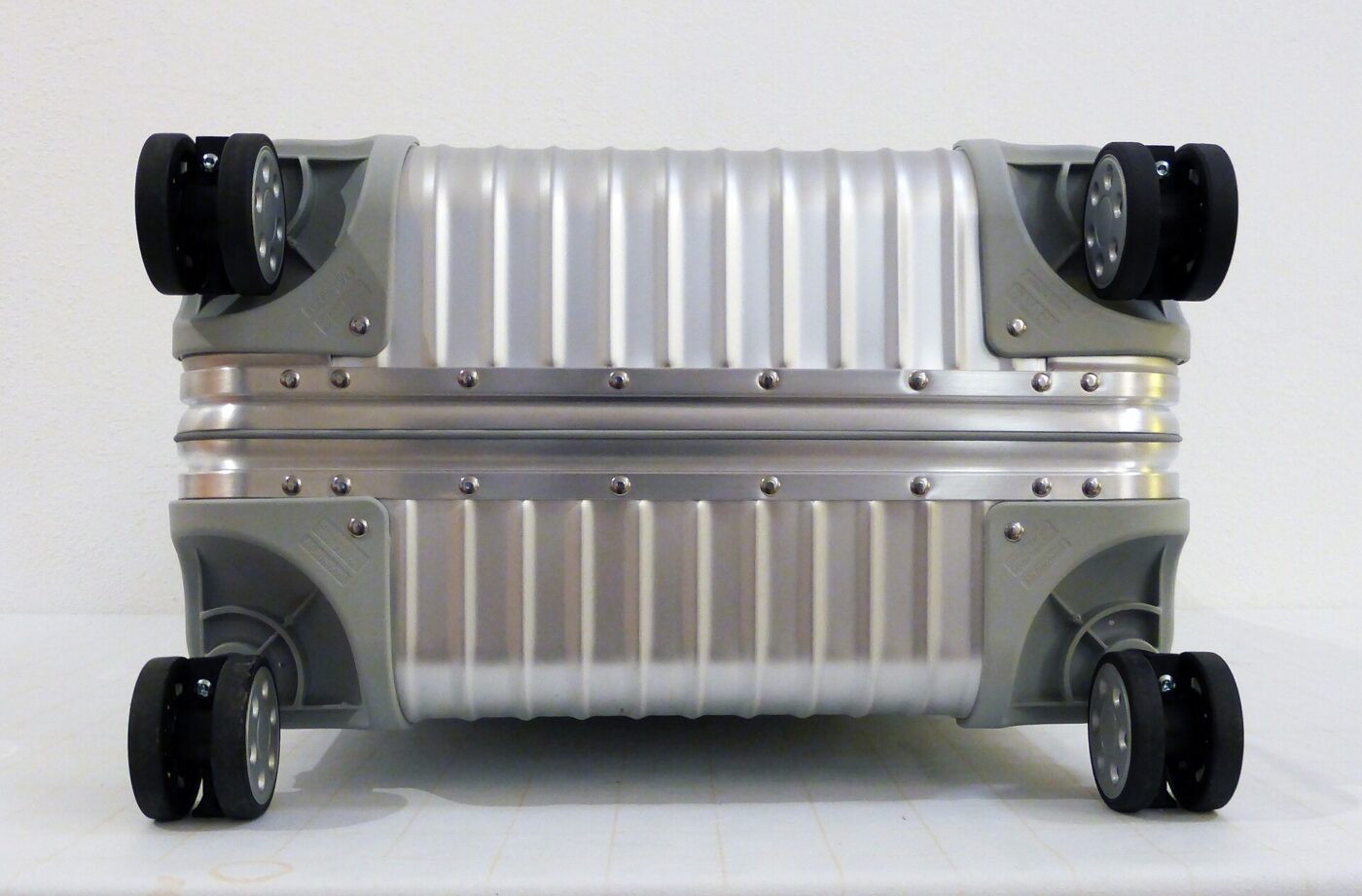 The underside of a Rimowa aluminium suitcase, showing its spinner wheels.