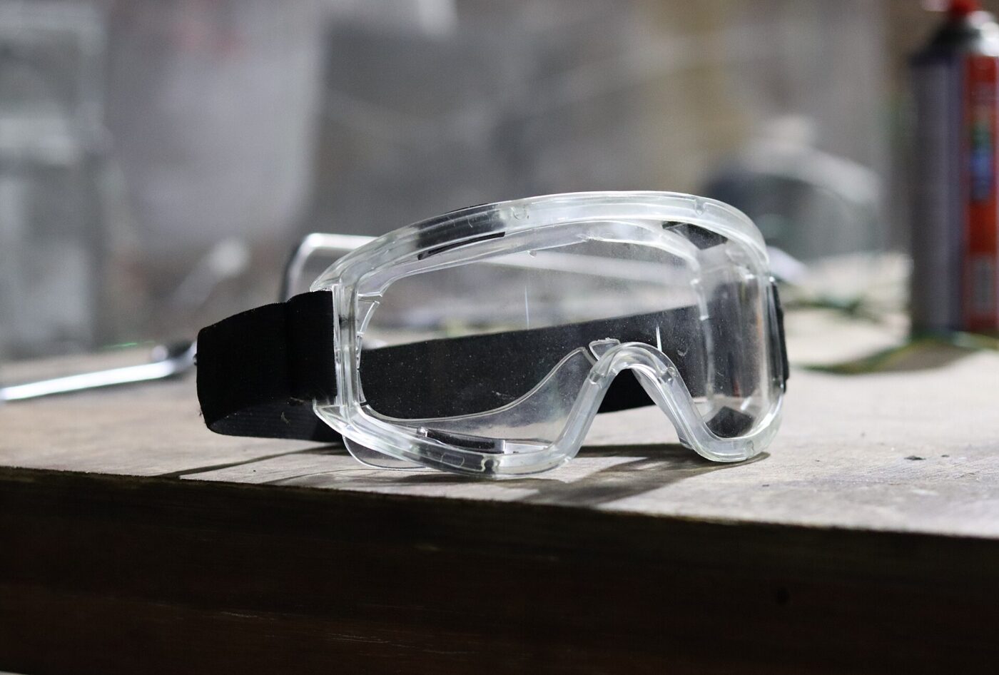 Clear protective safety goggles sitting on a wood table.