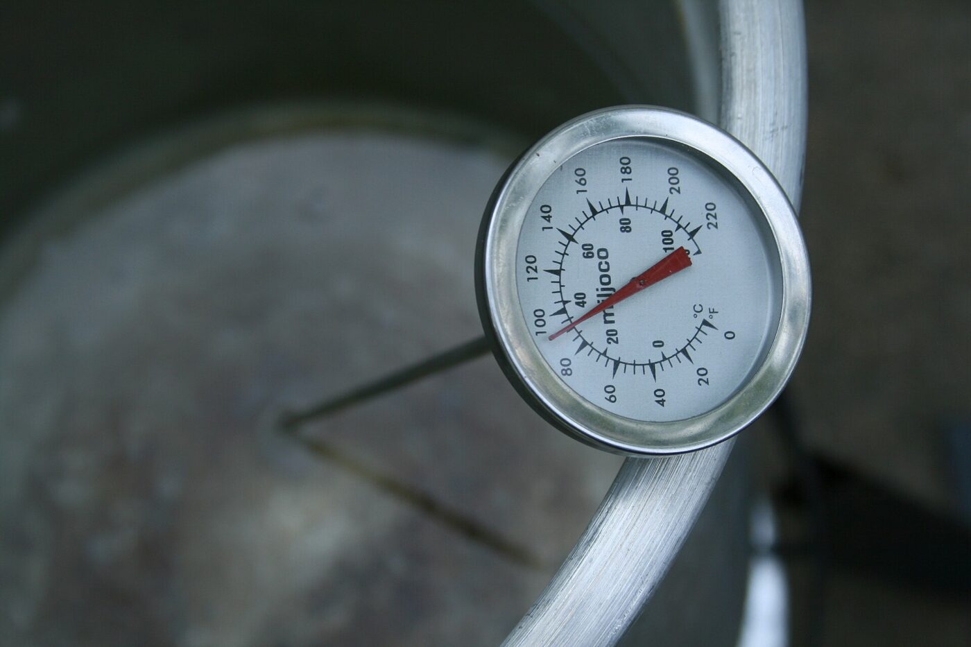 Close-up of a round dial meat thermometer inserted into food cooking on a grill.
